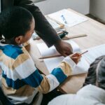 Crop black female helping ethnic boy and girl with assignment while studying in school classroom