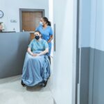 Nurse assisting a patient in a wheelchair at a medical facility reception.