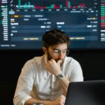 Pensive businessman with a beard analyzing stock market trends on a laptop in an office setting.